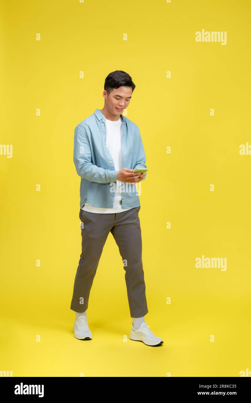 Happy man in casual wear using mobile phone chatting online, walking on yellow background Stock Photo