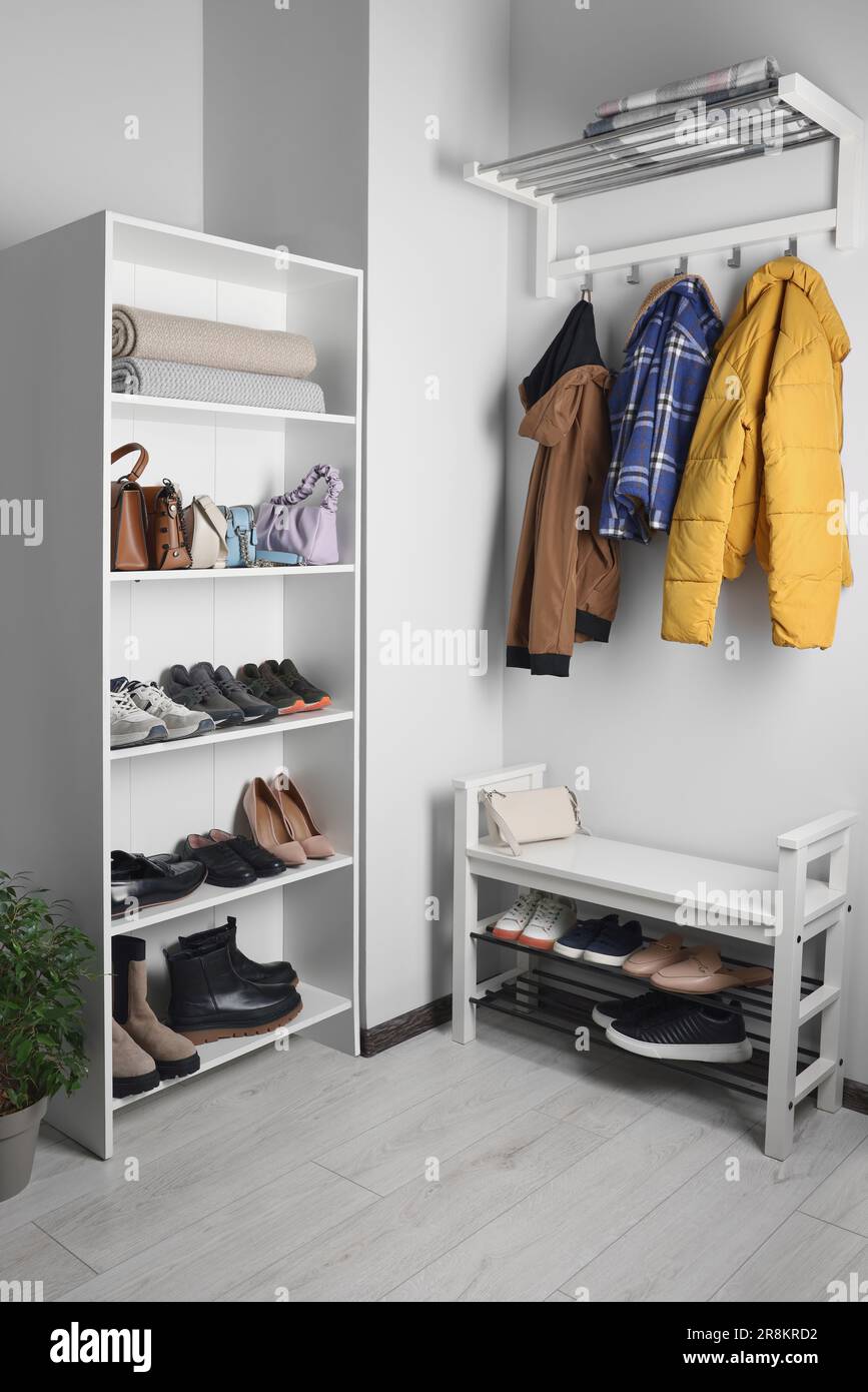 Shelving unit, coat rack and shoe storage bench near white wall in