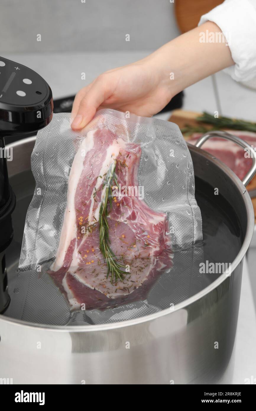 Woman putting vacuum packed meat into pot with sous vide cooker in