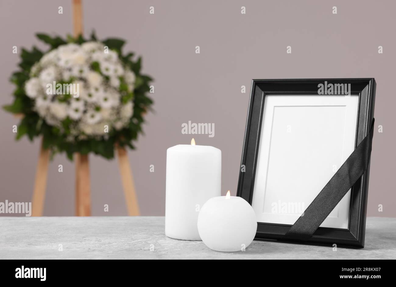 Photo frame with black ribbon, burning candles on table and wreath of