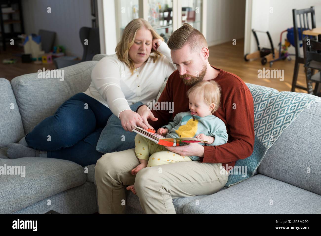 Parents with baby with down syndrome reading a book on sofa in living