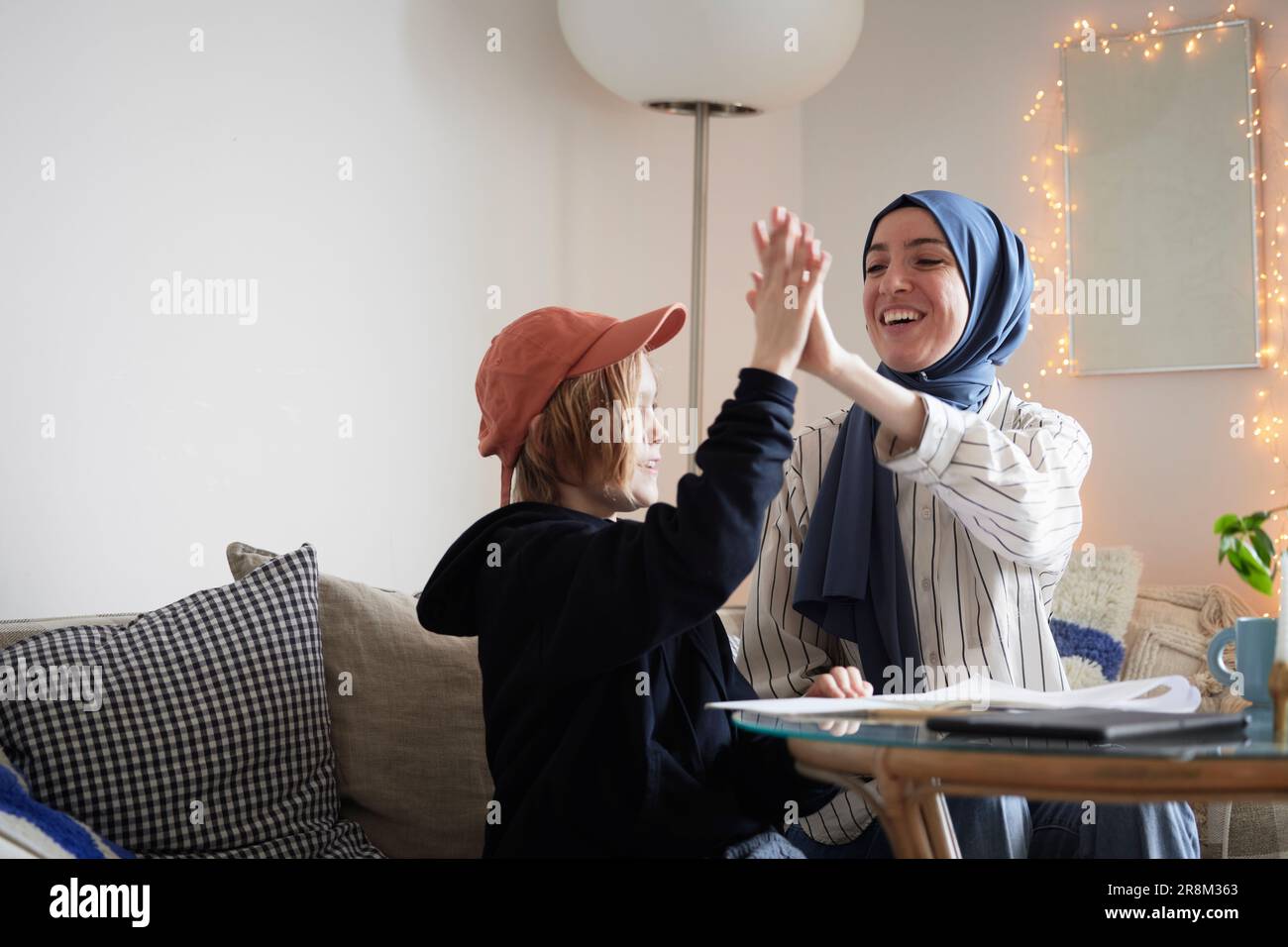 Mother wearing hijab helping son doing homework and doing high five Stock Photo