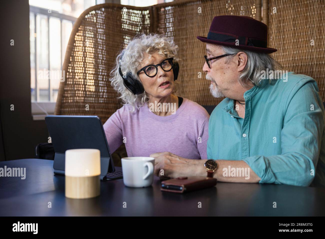 Senior couple sitting in cafe talking while working on digital tablet Stock Photo