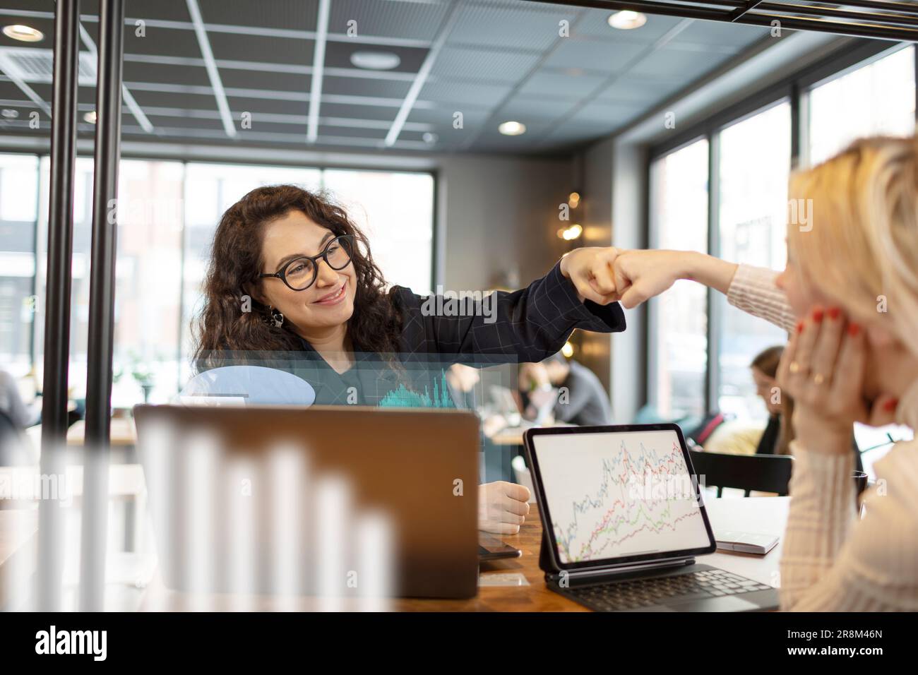 Smiling woman giving fist bump to colleagues in office Stock Photo