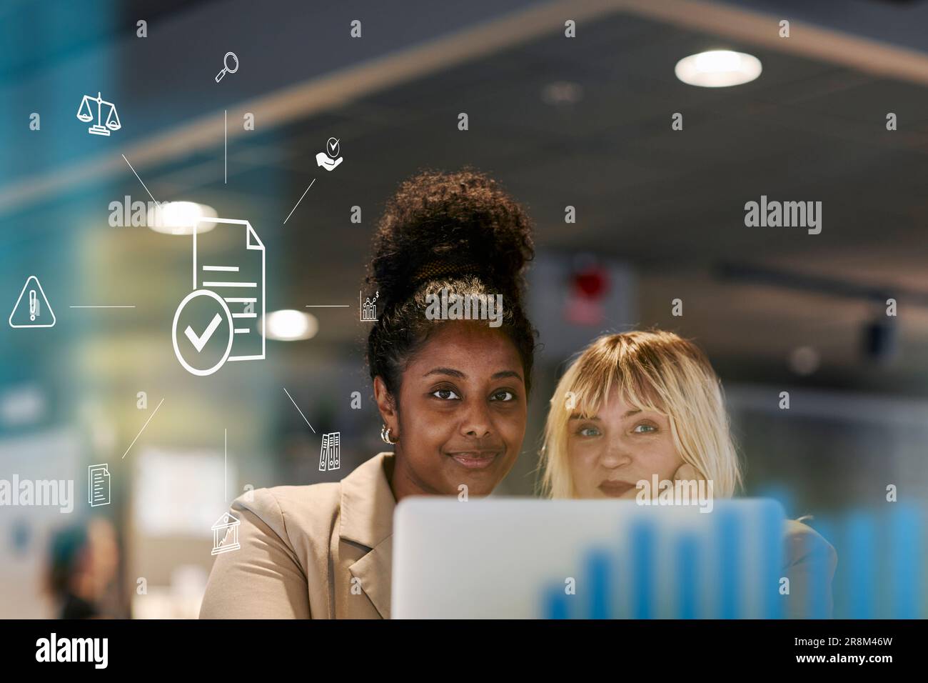 Smiling female colleagues in office, document computer icon in foreground Stock Photo