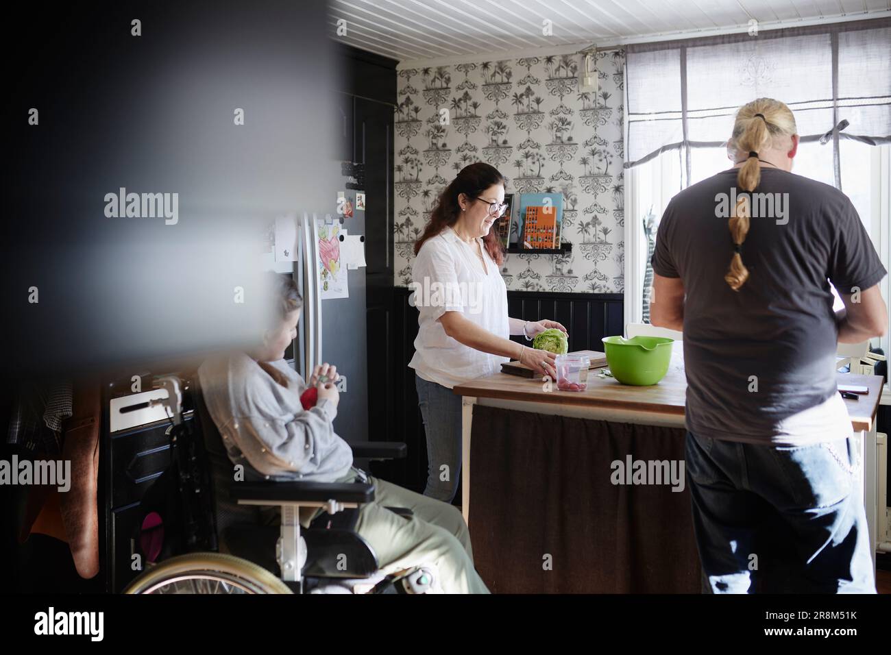 Parents with disabled daughter in wheelchair preparing food in kitchen Stock Photo