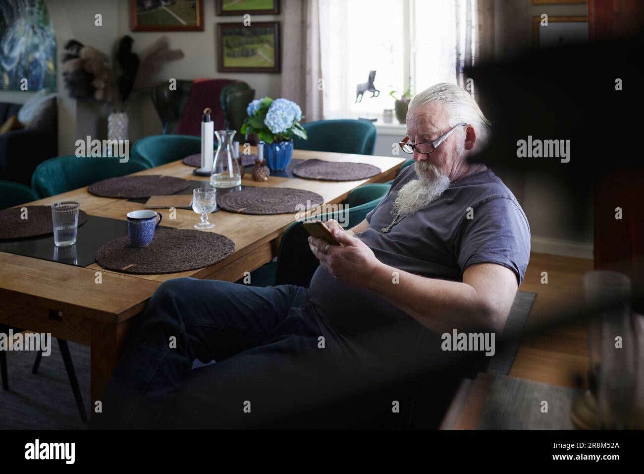 Mature man sitting at dining table and using cell phone Stock Photo