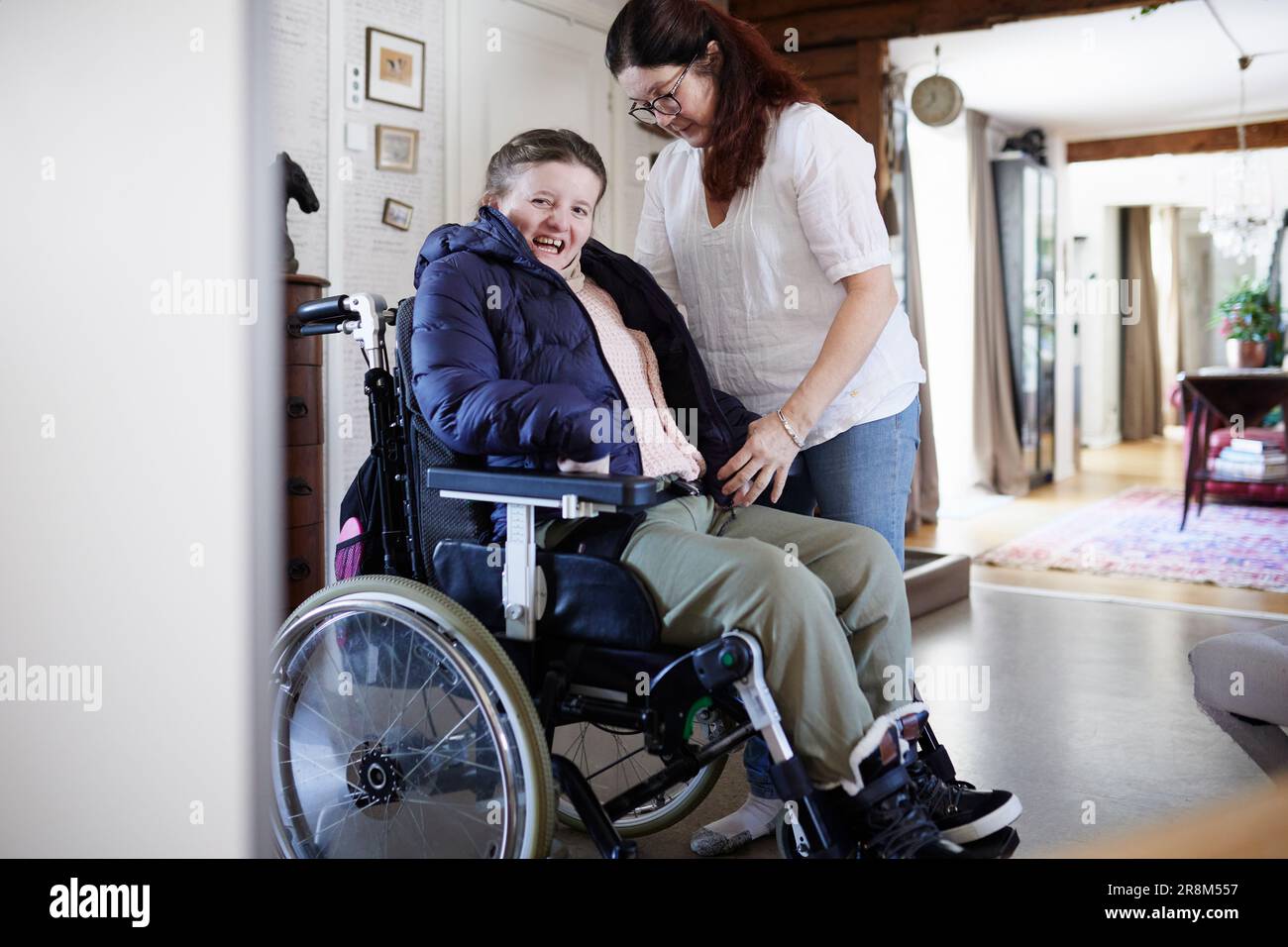 Mother helping disabled daughter in wheelchair putting coat on Stock