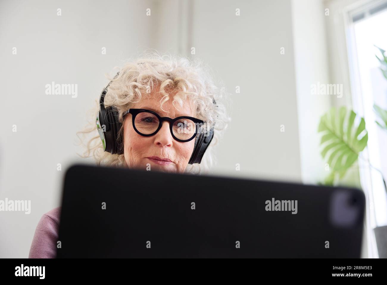 Smiling senior woman sitting withe headphones on and using laptop Stock Photo