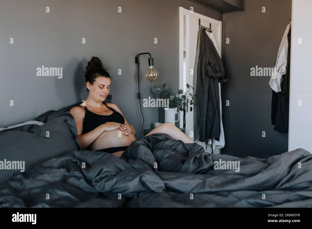 Pregnant woman relaxing in bed and touching belly with care Stock Photo
