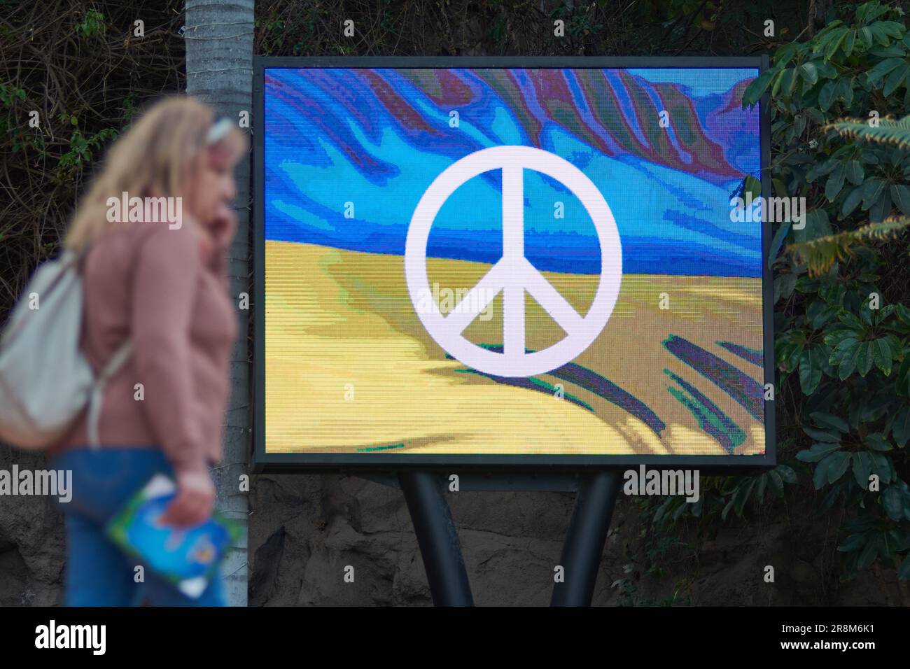 Tenerife, Spain - June 22, 2023: Unrecognizable woman talking on the phone next to a monitor with the Ukrainian flag and the peace sign superimposed Stock Photo