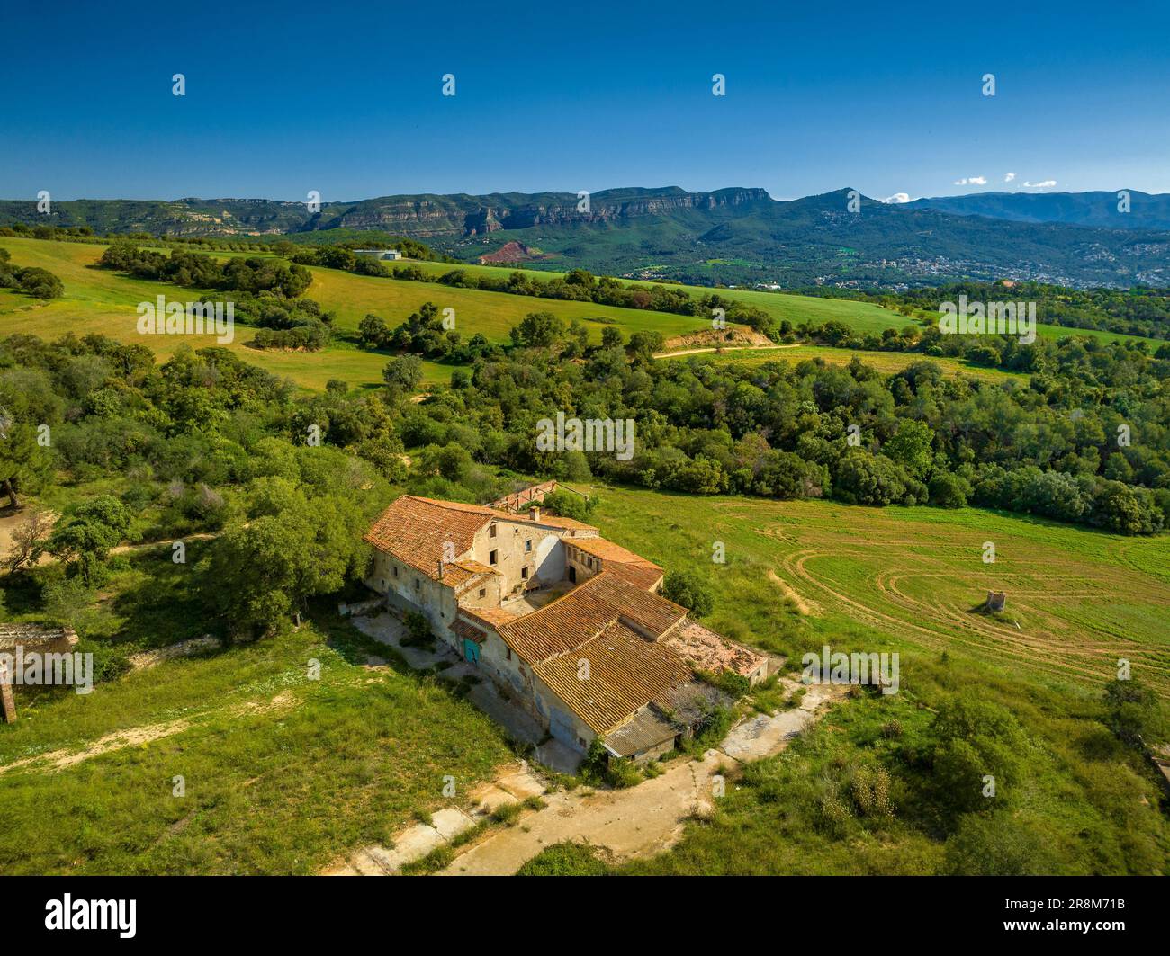 Can Rosàs farmhouse and its green rural surroundings in spring, in Santa Eulàlia de Ronçana. In the background, the Cingles de Bertí mountains (Spain) Stock Photo