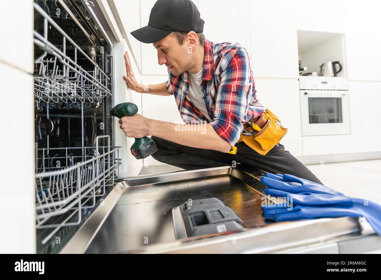 Worker using screwdriver to repair dishwasher at home stock photo Stock Photo