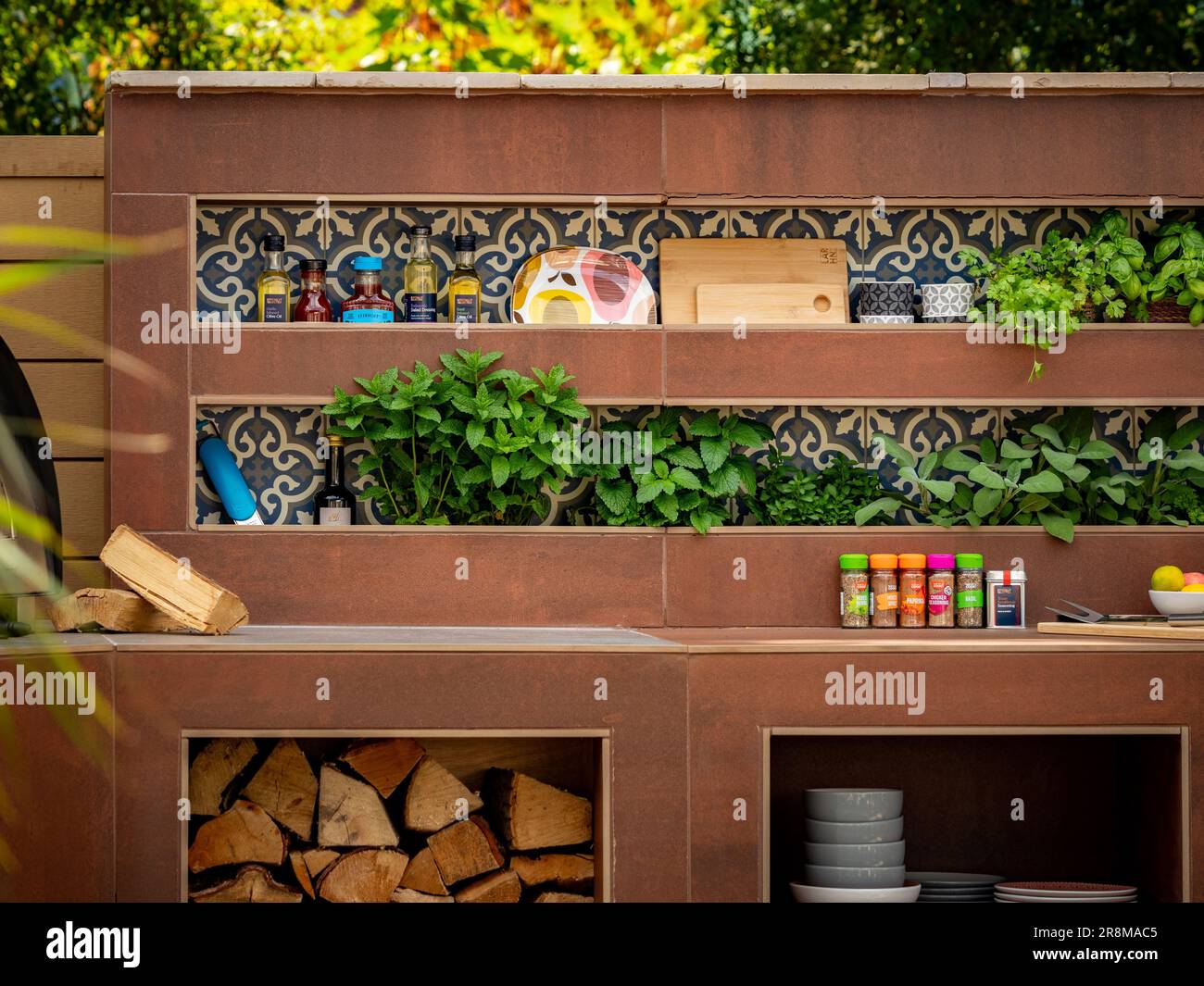 Outdoor kitchen complete with recessed shelves for storage of crockery, bottles of oil, and pots of herbs in a UK garden show Stock Photo