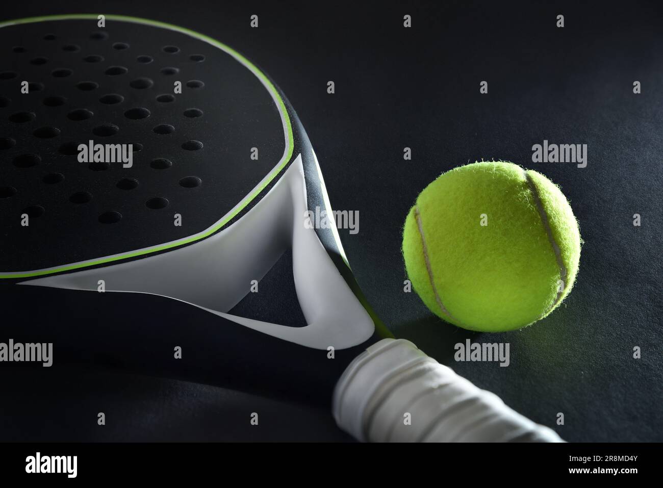 Detailed background of black and white padel racket and ball on black background. Elevated view. Stock Photo