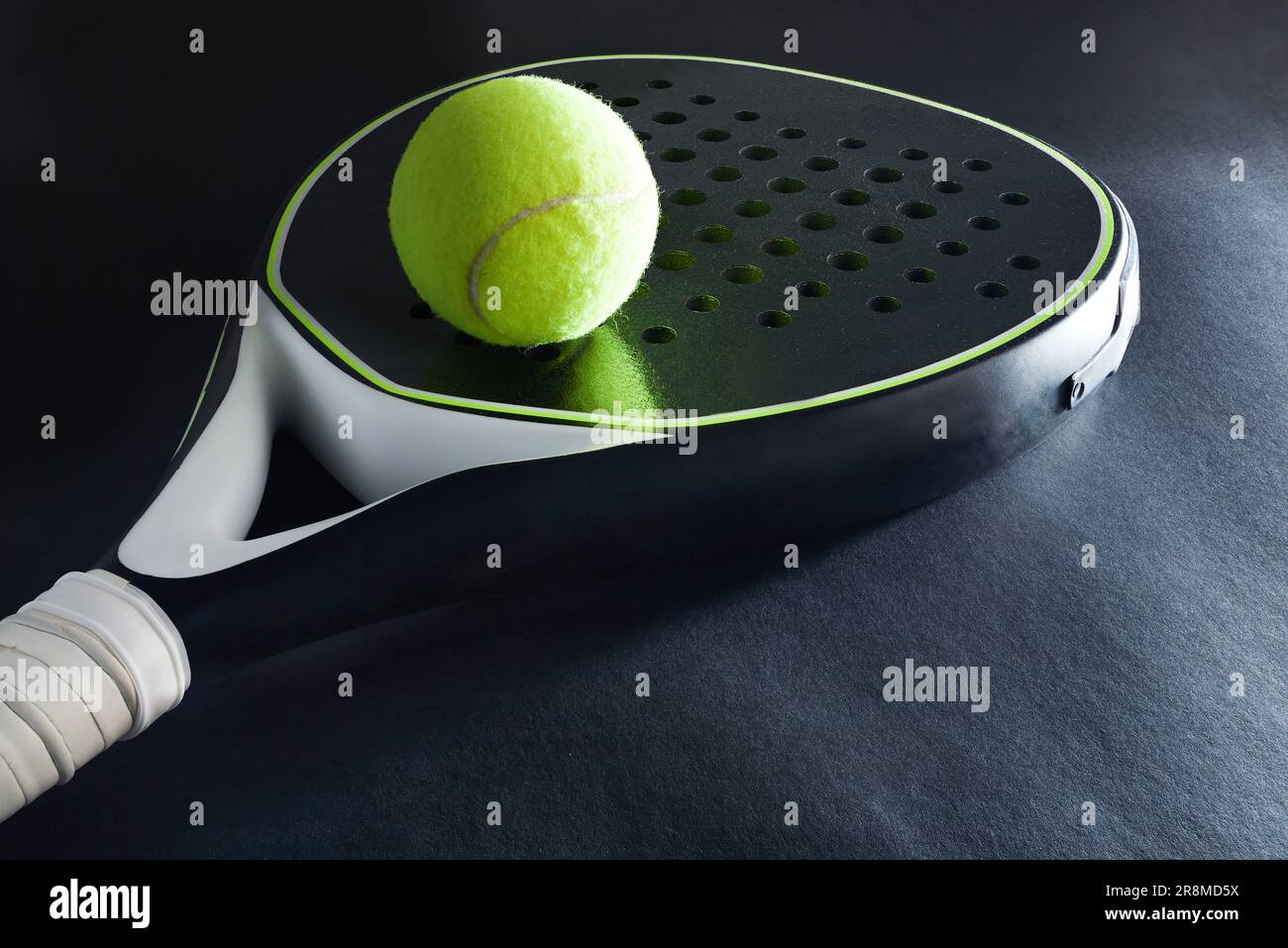 Background of black and white paddle racket and ball on top on black background. Elevated view. Stock Photo