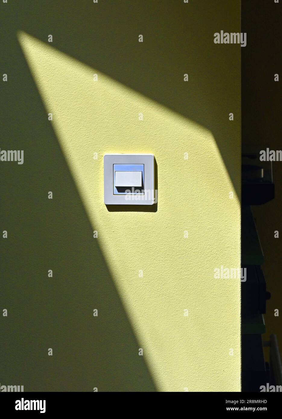 Electric Light Switch in sunlight on yellow wall with shadow. Stock Photo