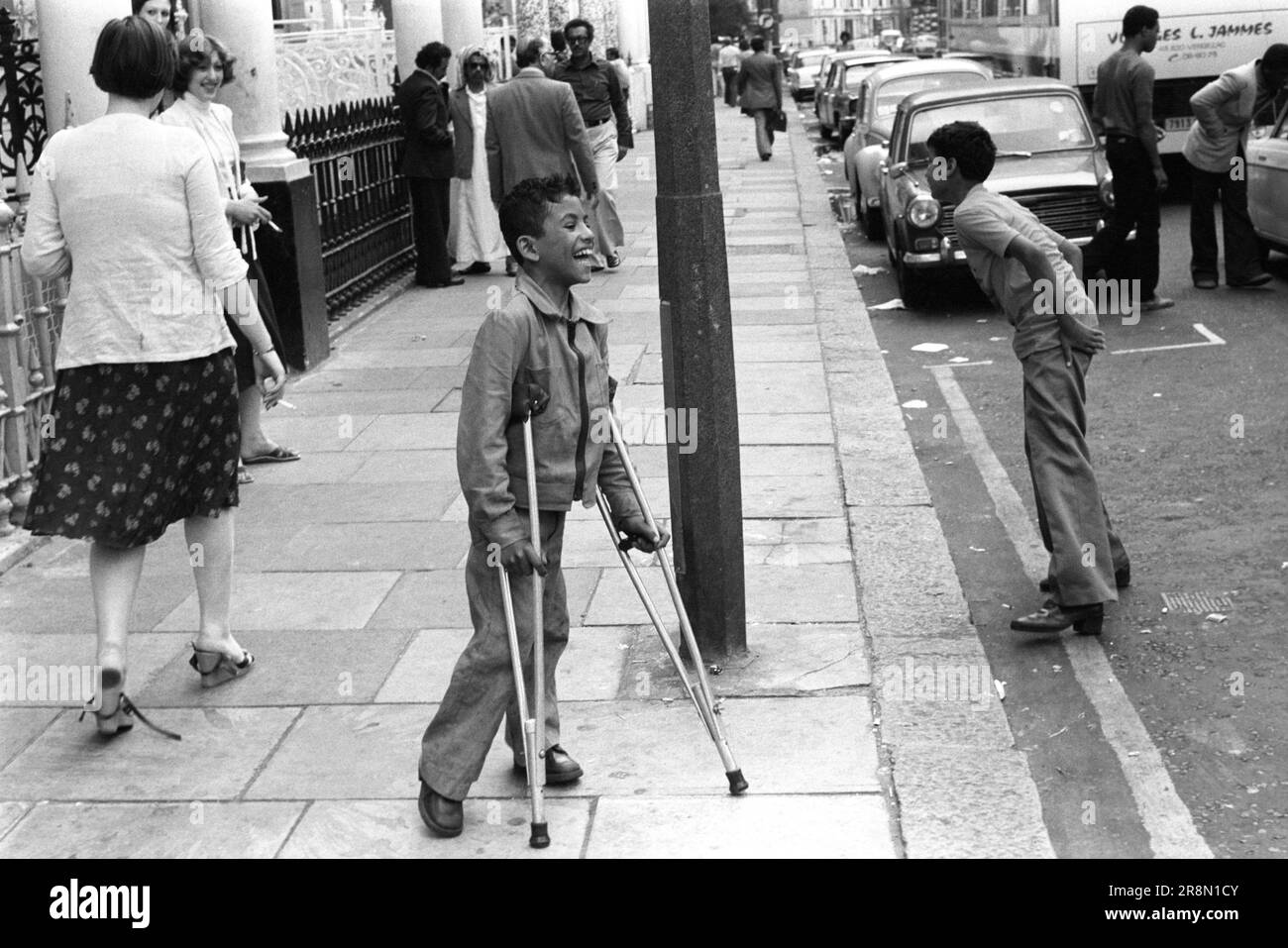 Arab children playing in street, one boy on crutches. Earls Court London 1970s.  Middle Eastern people came to Britain for subsidised health care in Harley Street clinics. They mainly stayed in cheap hotels in Earls Court. Middle Eastern children playing in the street. Earls Court, London, England circa 1977 70s UK HOMER SYKES Stock Photo