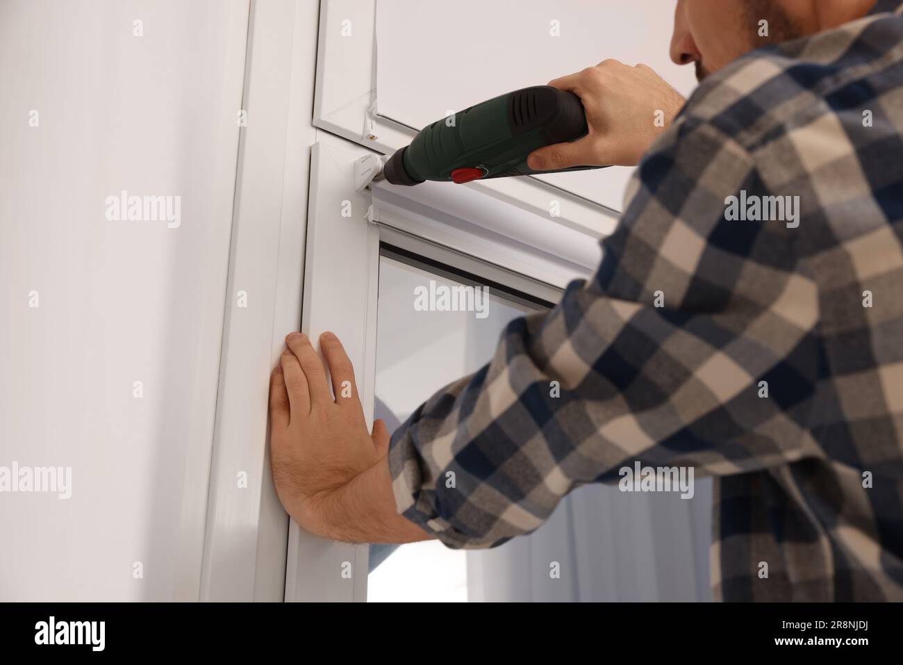 Man with drill installing roller window blind indoors, closeup Stock Photo