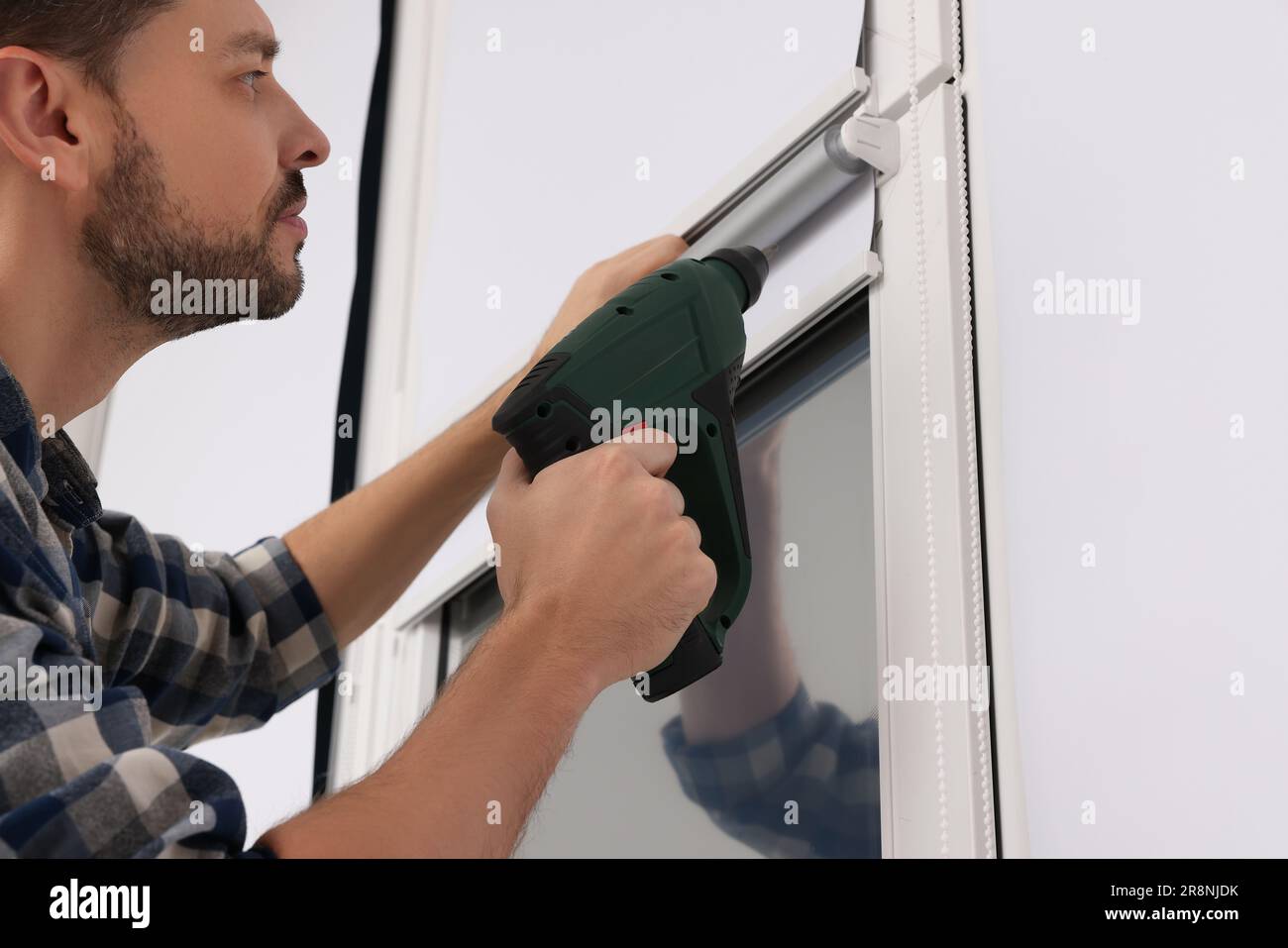 Man with drill installing roller window blind indoors, closeup Stock Photo