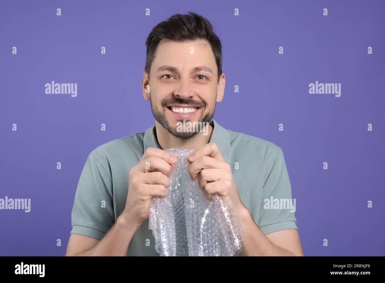 Happy man popping bubble wrap on purple background. Stress relief Stock