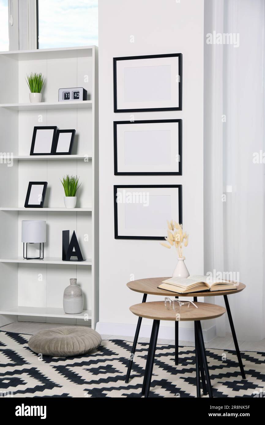 Stylish room interior with empty frames hanging on white wall near