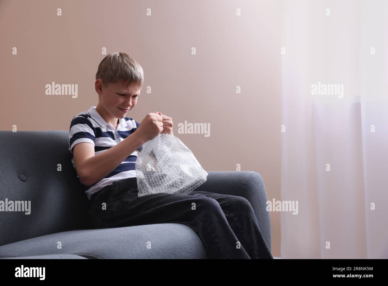 Emotional boy popping bubble wrap indoors. Stress relief Stock Photo