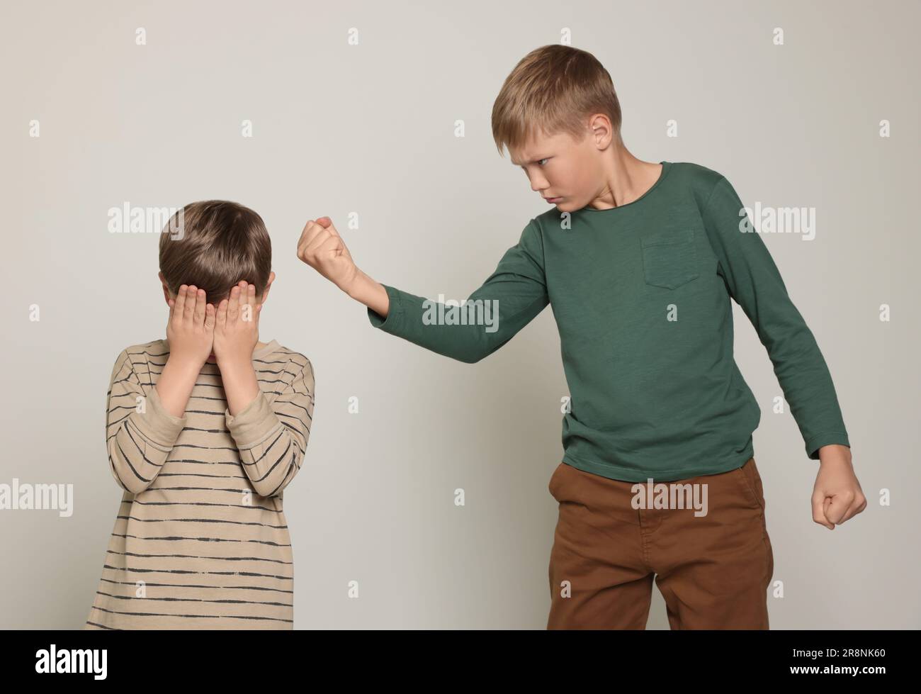 Boy with clenched fist looking at scared kid on light grey background
