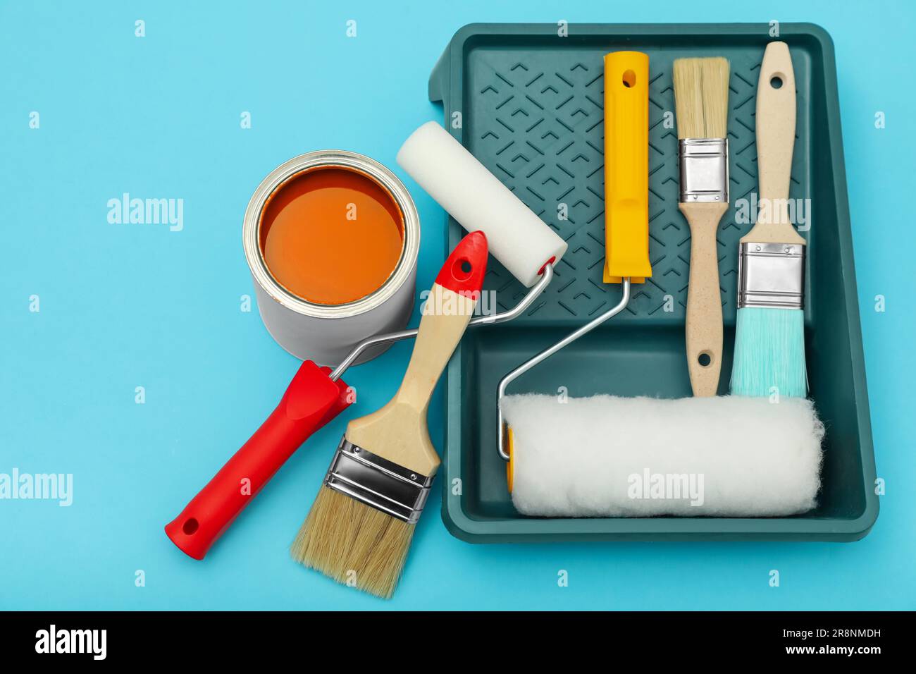 Can of orange paint, brushes, rollers and container on turquoise