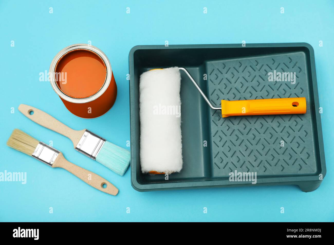 Can of orange paint, brushes, roller and container on turquoise