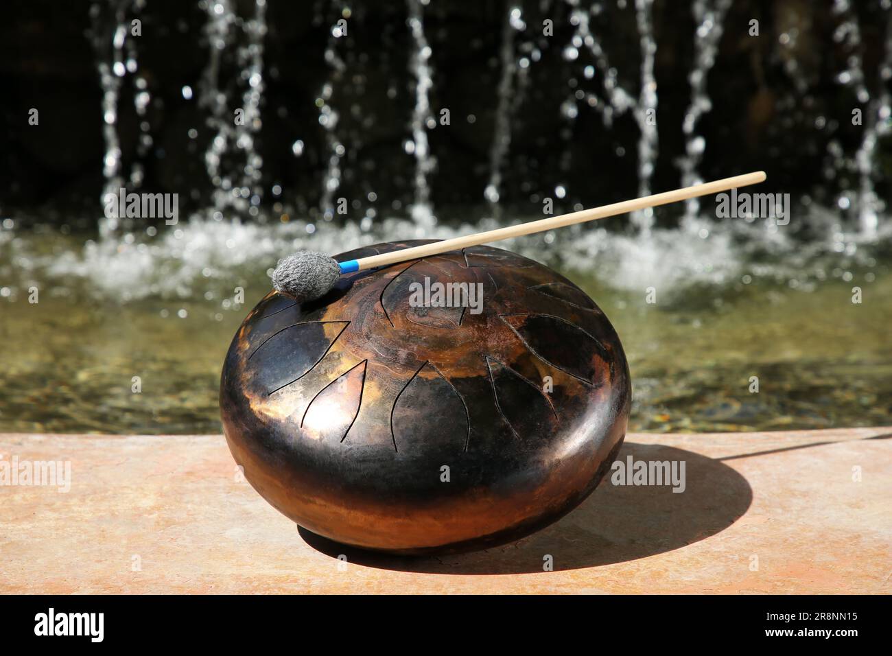 Steel tongue drum with mallet near waterfall outdoors on sunny day ...