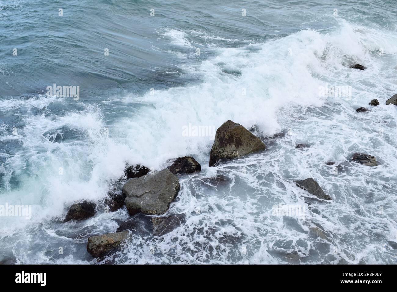 An idyllic landscape featuring a rocky shoreline with waves of the sea crashing against it, creating a tranquil atmosphere Stock Photo