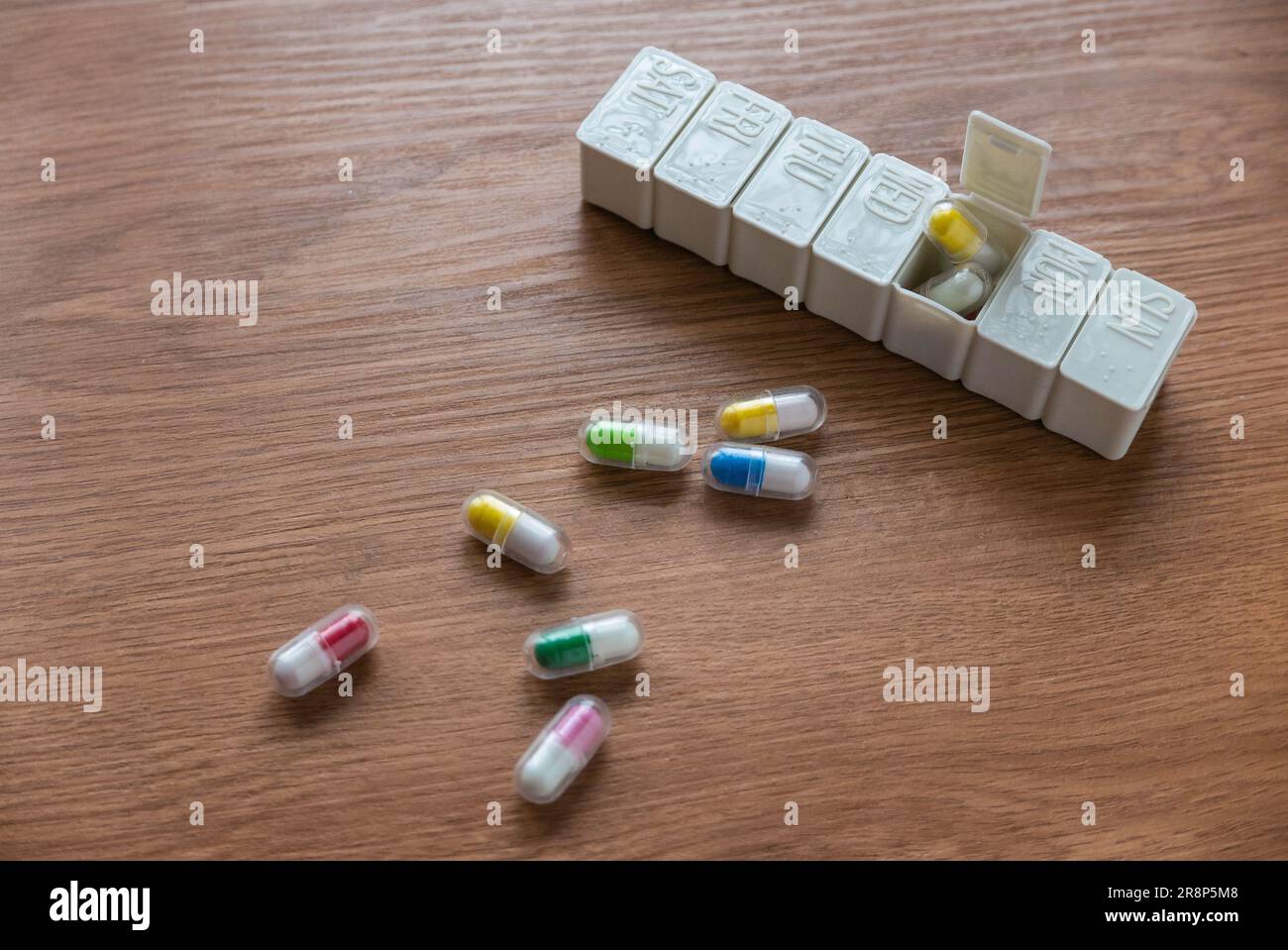 Selective focus of pill box with spilled pills on wooden table. Stock Photo