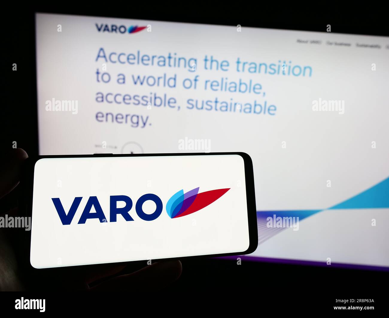 Person holding smartphone with logo of Swiss company VARO Energy Marketing AG on screen in front of website. Focus on phone display. Stock Photo
