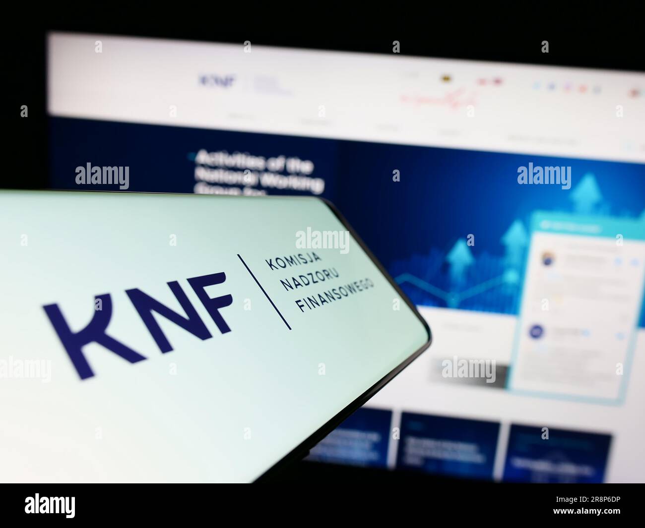 Mobile phone with logo of authority Komisja Nadzoru Finansowego (KNF) on screen in front of website. Focus on center-right of phone display. Stock Photo