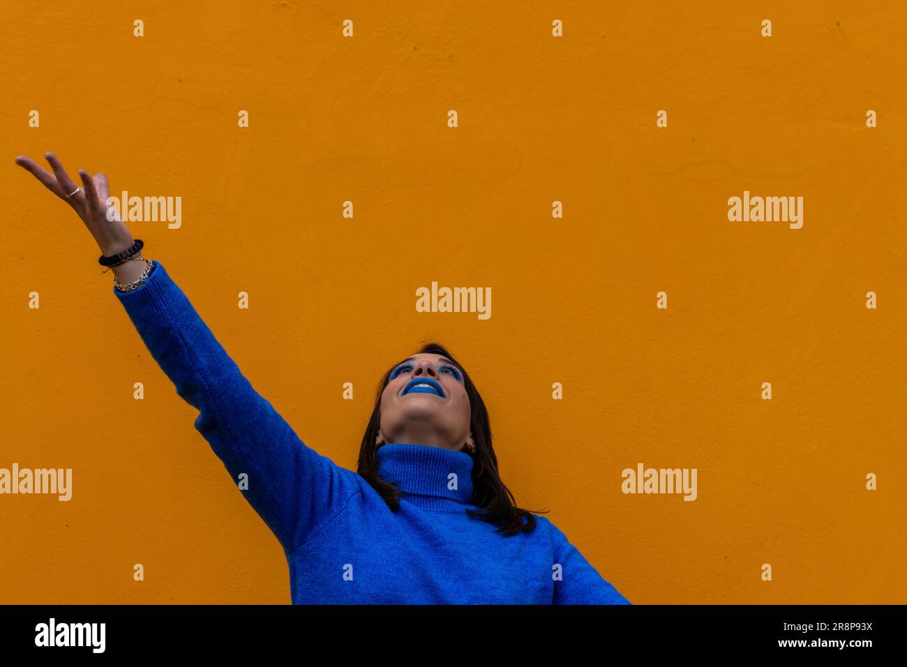A young woman wearing a blue shirt stands in front of a bright yellow ...