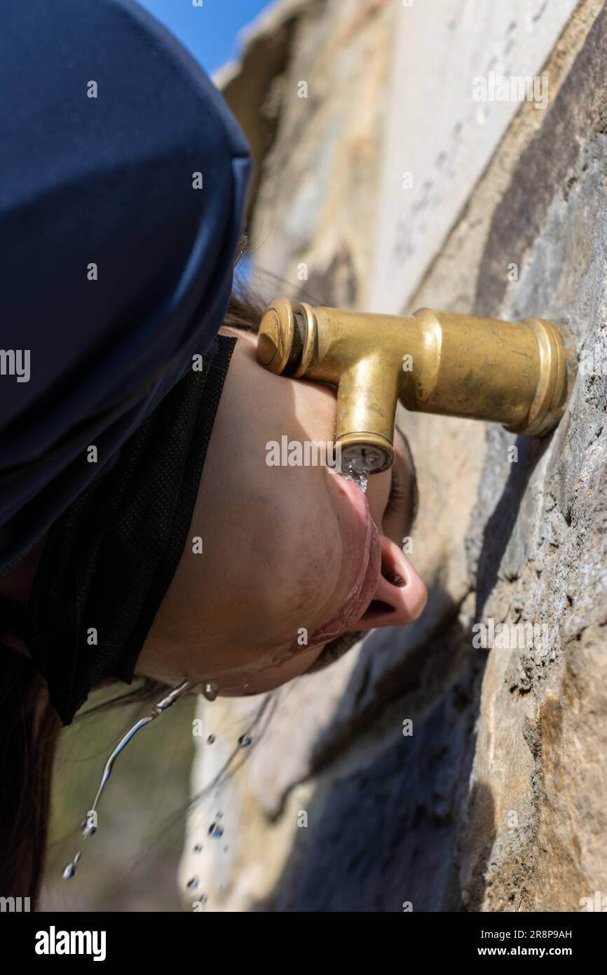 A mature male opening a metal water spout from a brick wall, revealing a stream of fresh water Stock Photo