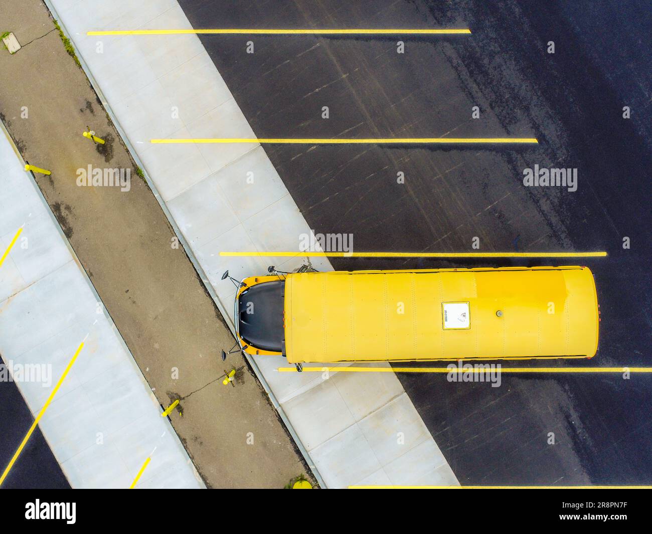 Aerial view of a single, one, yellow american school bus parking in a bus parking lot with concrete and asphalt surface. Stock Photo