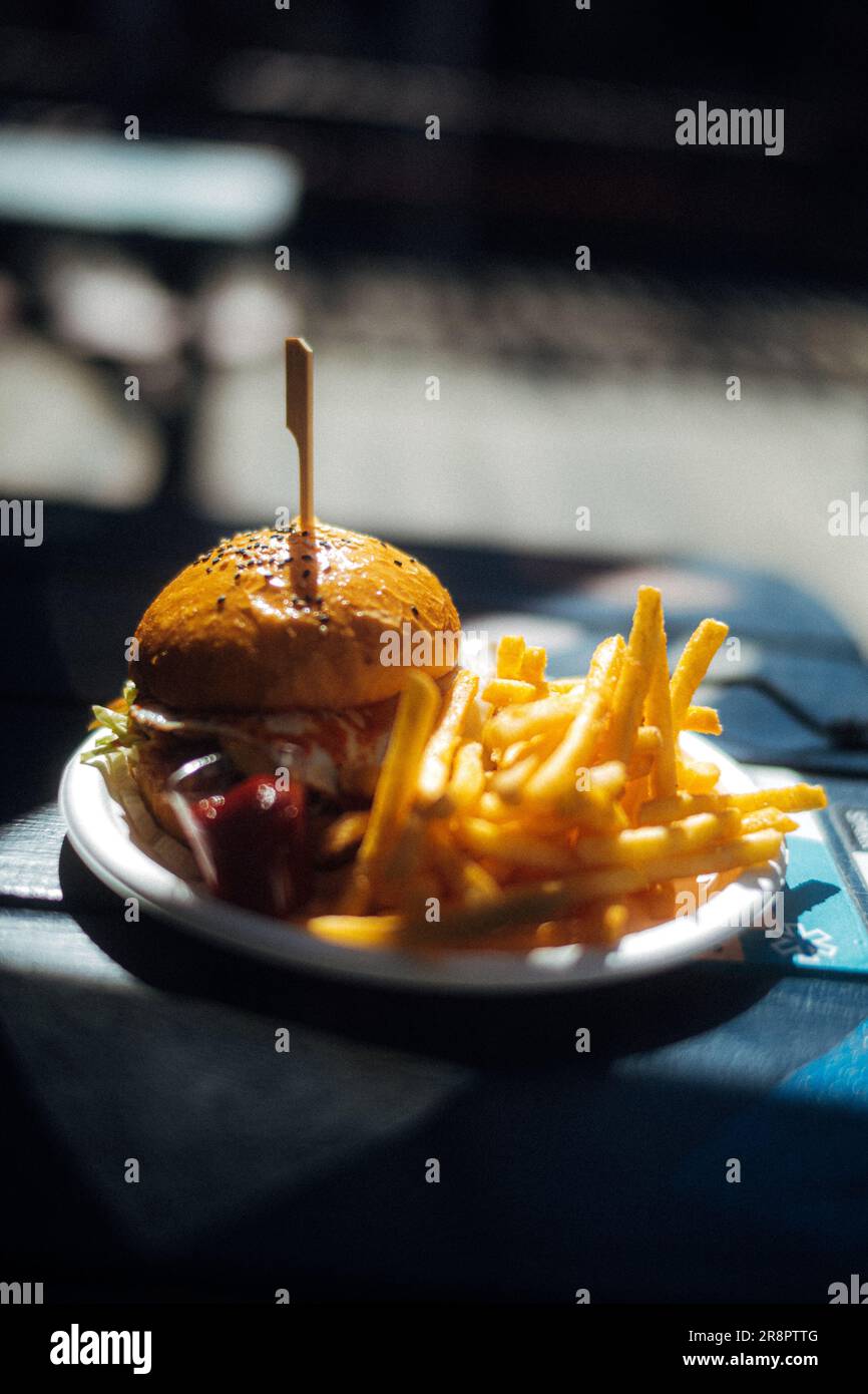 This image depicts a plate of food featuring a hamburger and french fries on a table Stock Photo