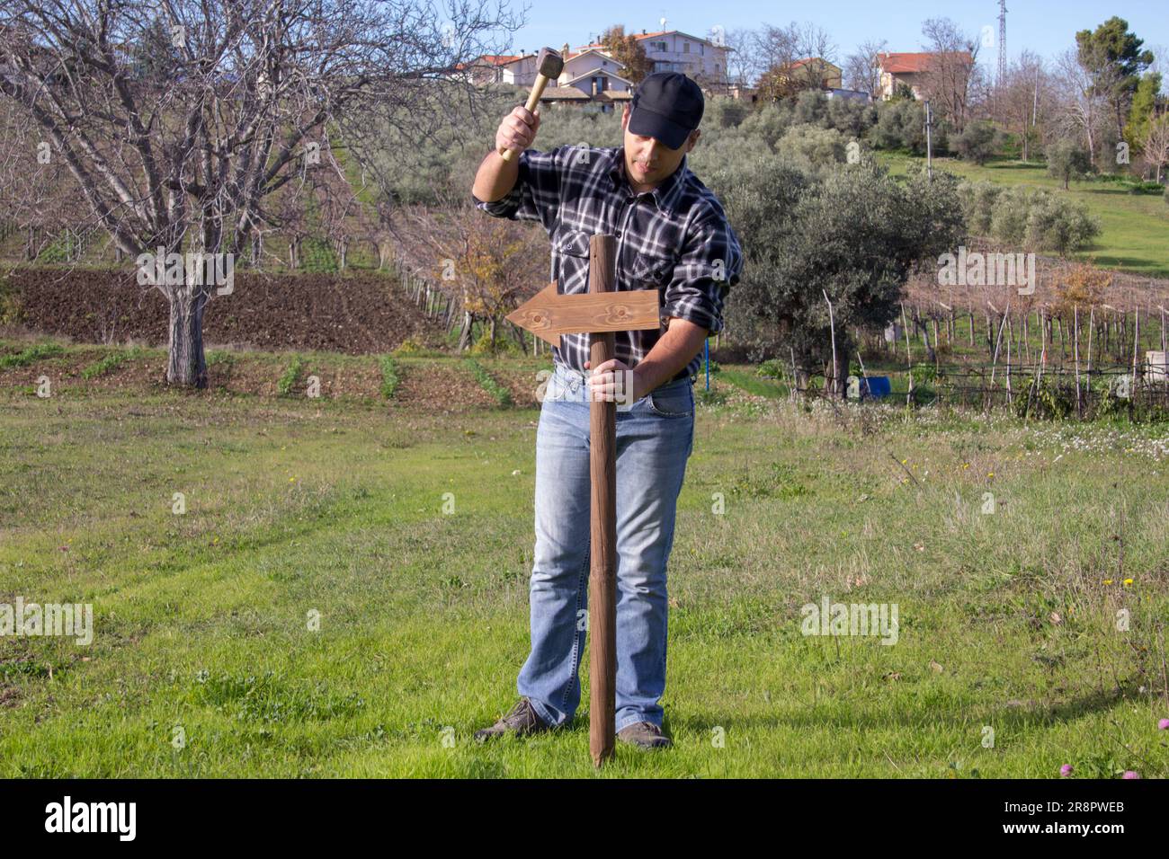 Image of a man driving a stake with an arrow into the ground with a hammer. Pole indicating the direction to take. Stock Photo