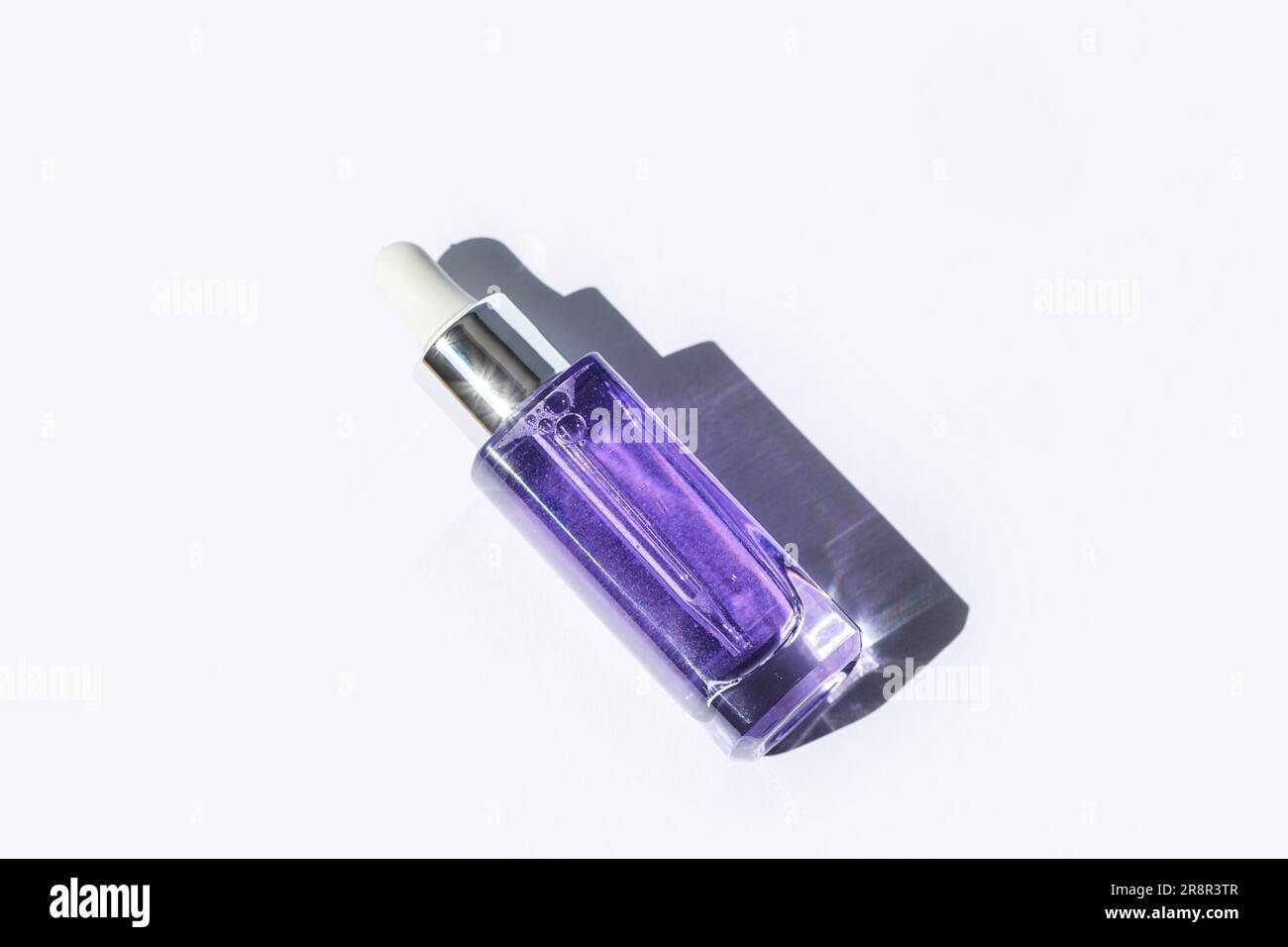 Purple cosmetic serum bottle with hard shadow on white background