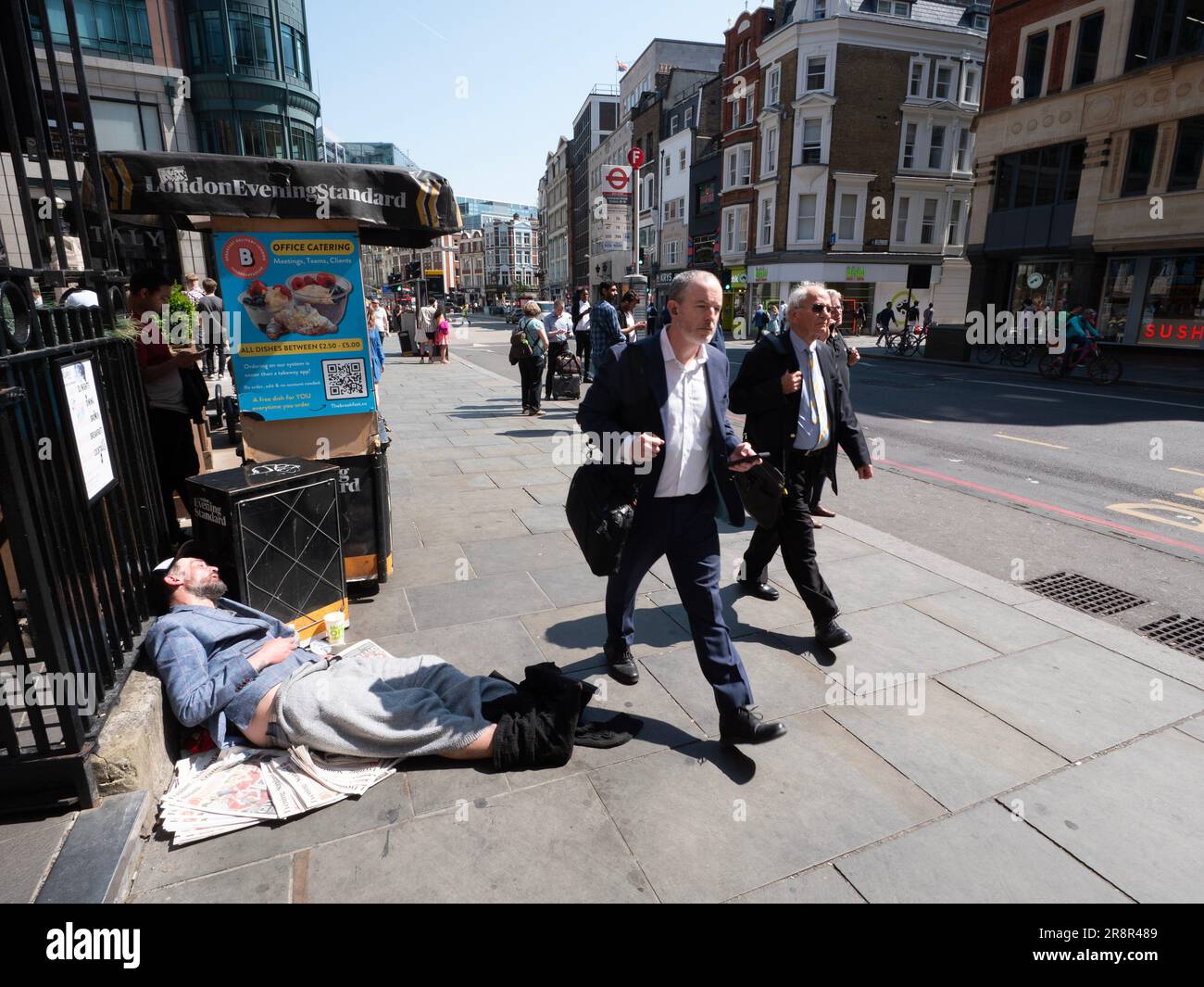 Suited commuters walking past sleeping homeless man at  Liverpool street Station London Stock Photo