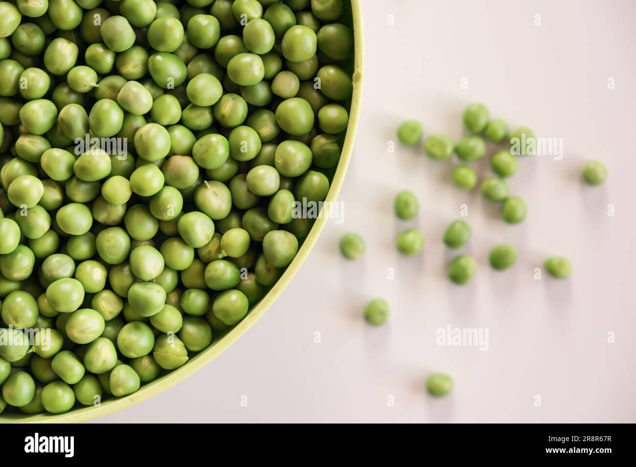 Fresh green garden peas in a green bowl isolated on white. Top view. Stock Photo