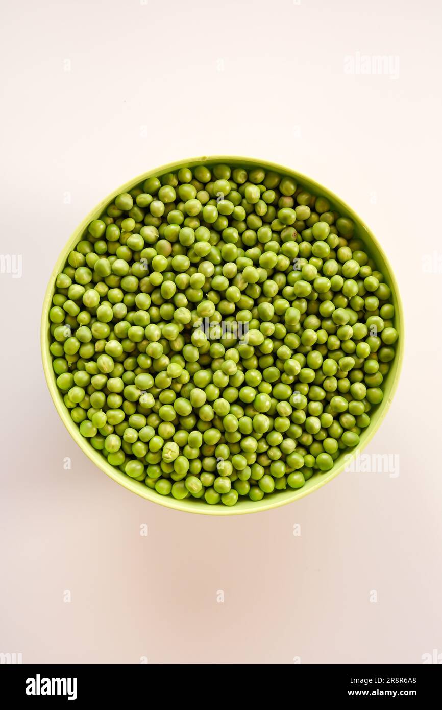 Fresh green garden peas in a green bowl isolated on white. Top view. Stock Photo