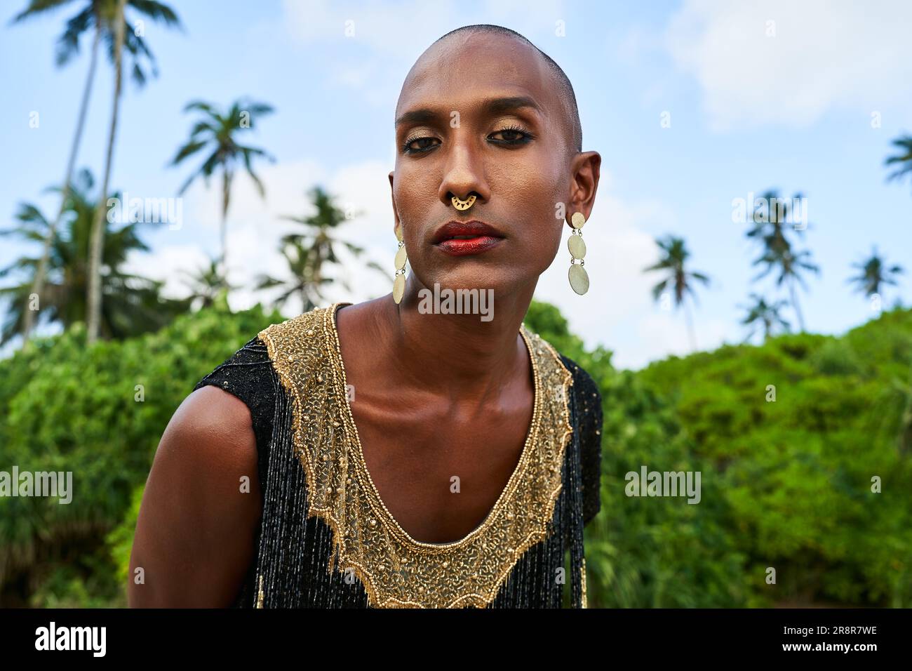 Flamboyant gay black man with luxury golden jewelry poses on scenic ocean  beach. Gender fluid ethnic fashion model brass rings, bracelet, earrings,  accessories looks stands with sophisticated posture. Stock Photo | Adobe