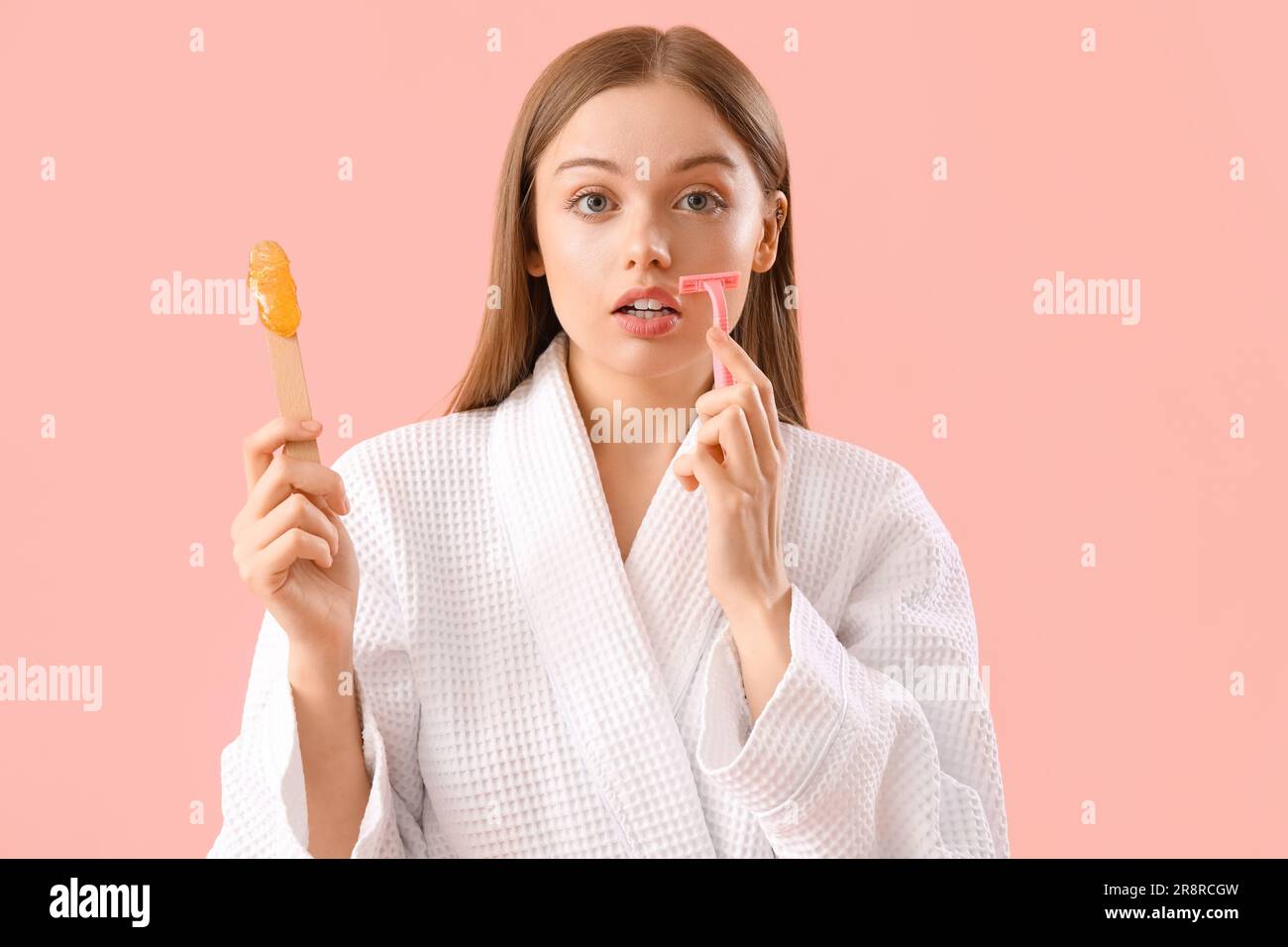 Young woman holding spatula with sugaring paste and razor on pink background Stock Photo