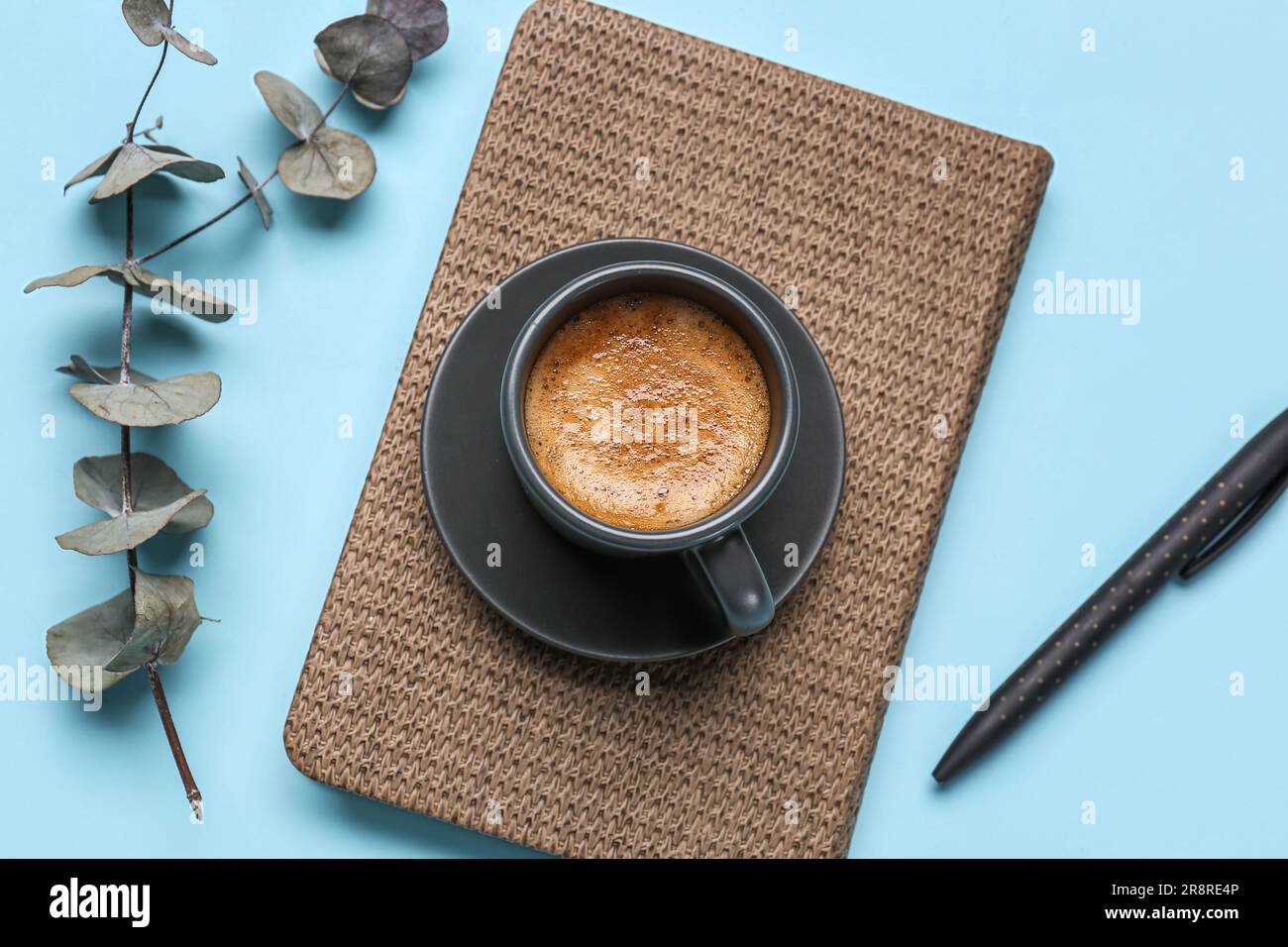 Cup of hot espresso, notebook, pen and eucalyptus branch on blue background Stock Photo