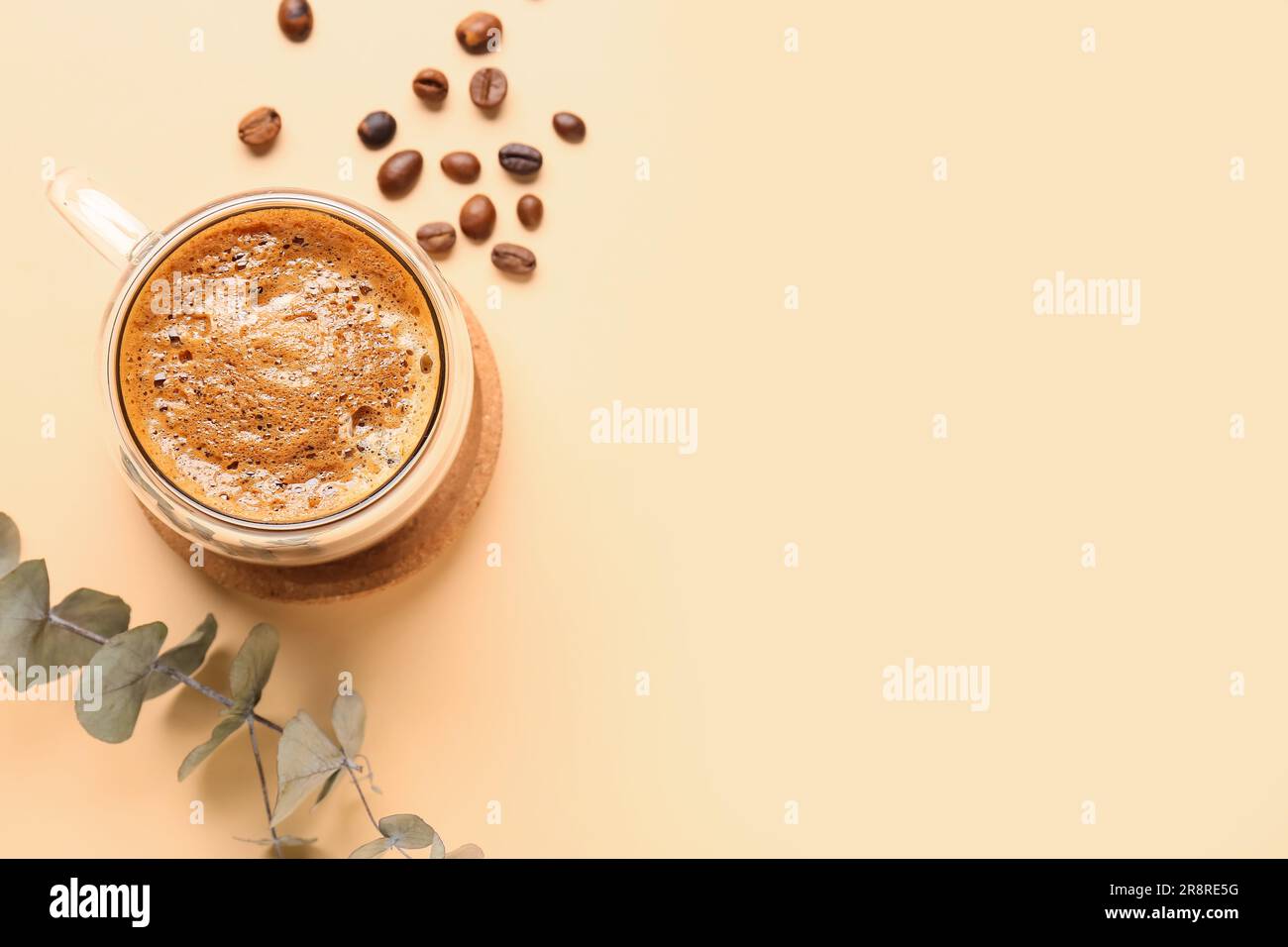 Glass cup of hot espresso and coffee beans with eucalyptus on beige background Stock Photo