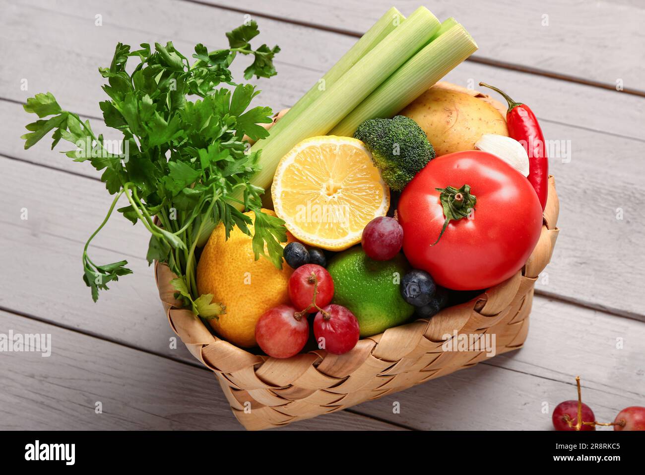 Wicker basket with different fresh fruits and vegetables on grey wooden ...