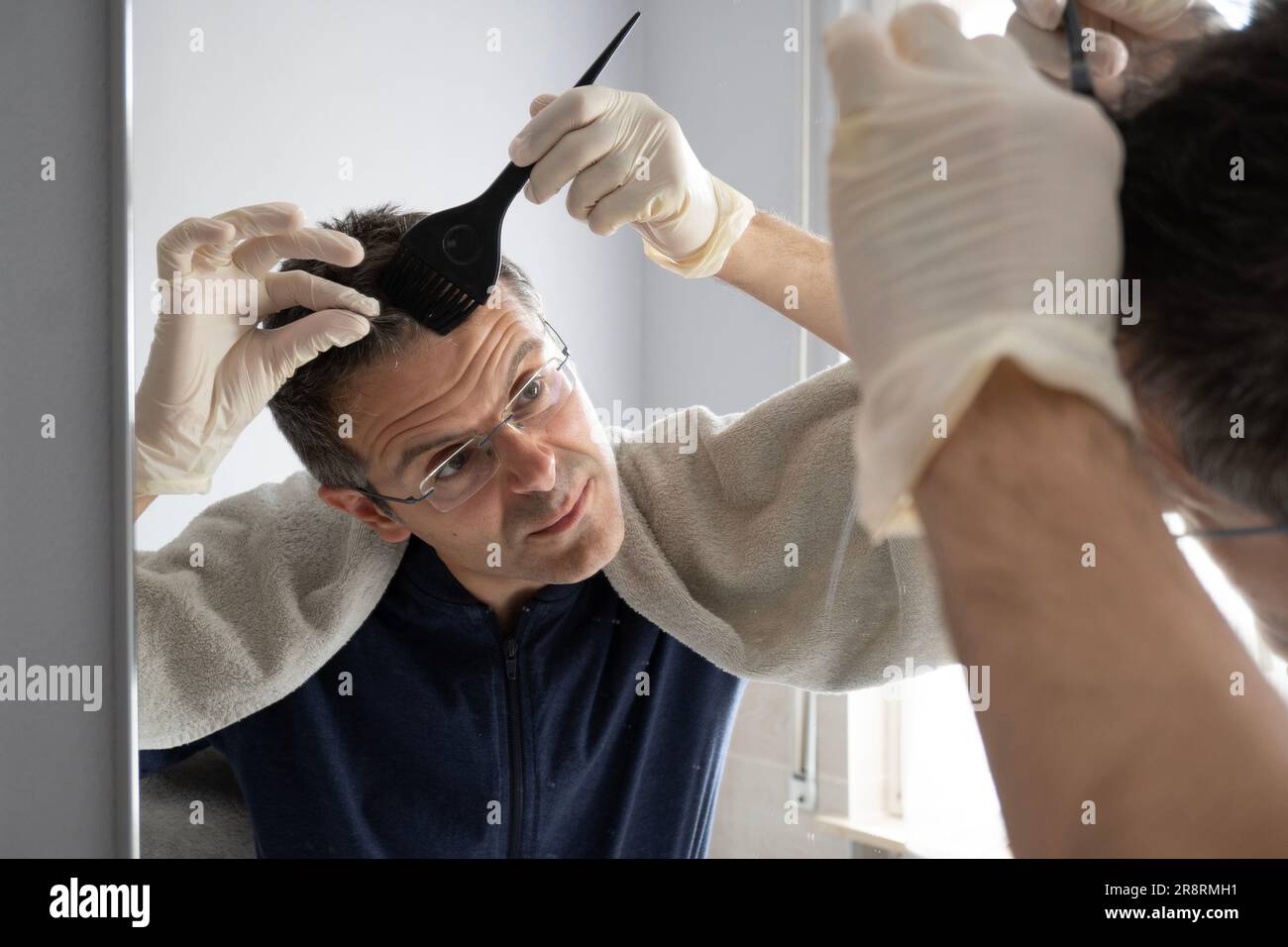Middle-aged man with white hair is dyeing his hair in the mirror Stock Photo